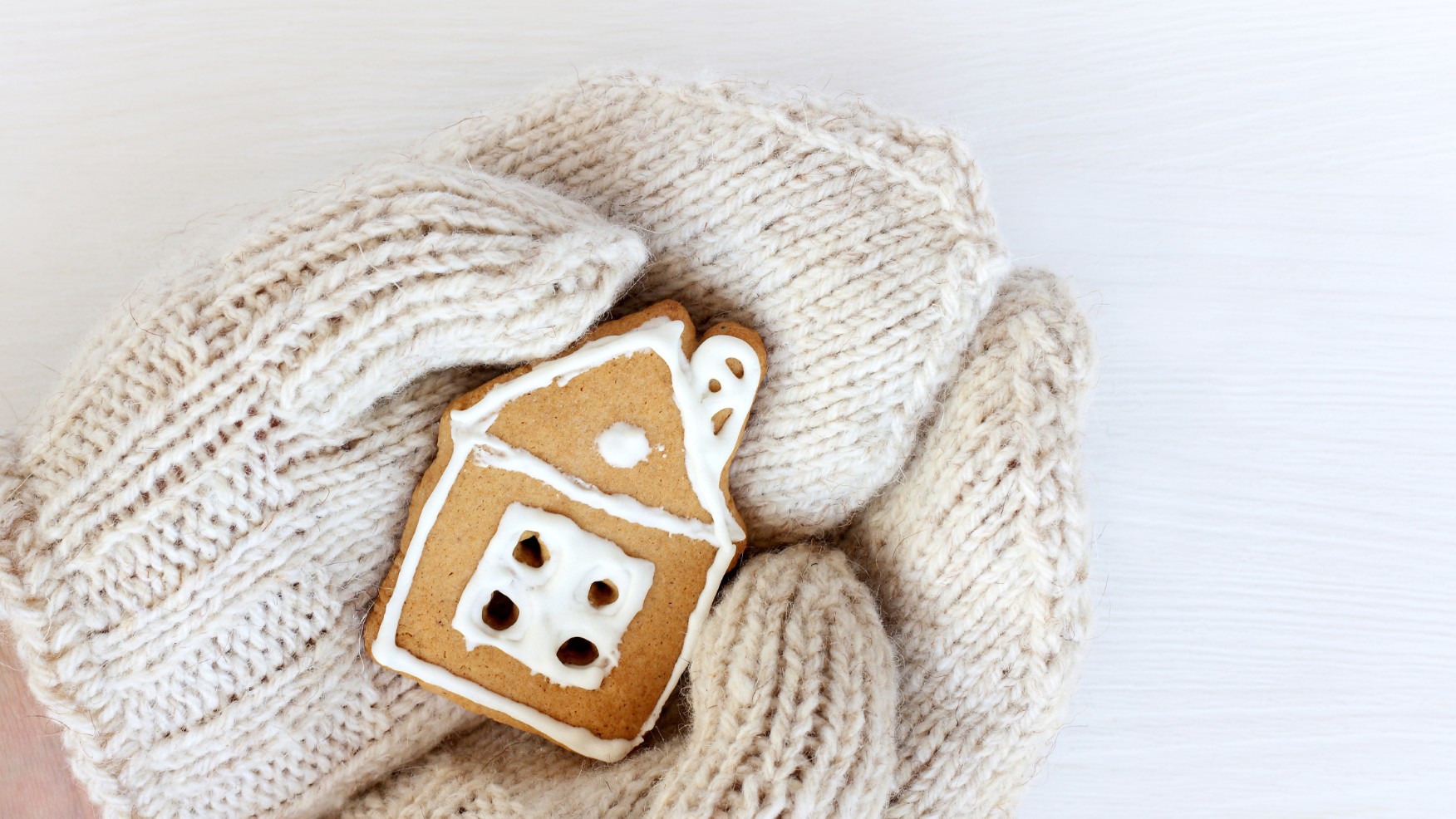 A house-shaped gingerbread cookie held in mittened hands